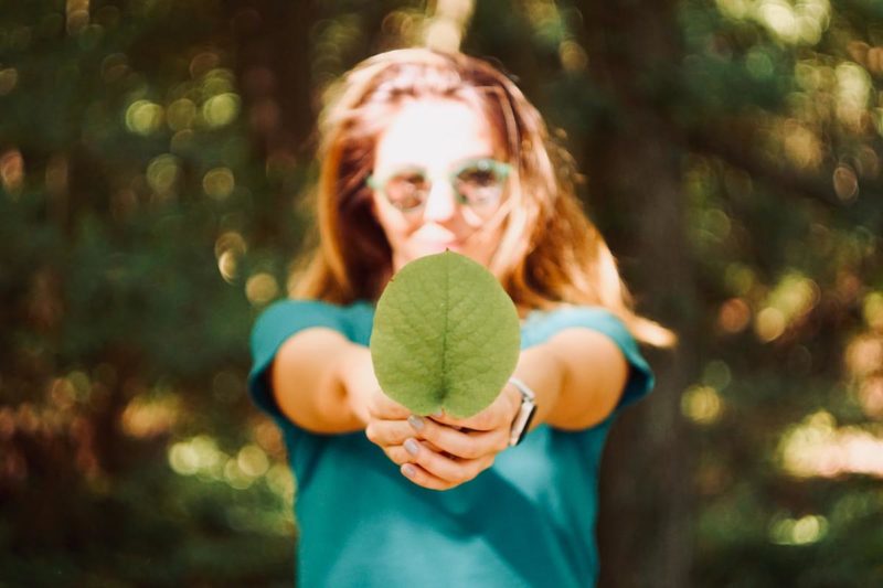 Jonge vrouw met groen boomblad in haar hand.