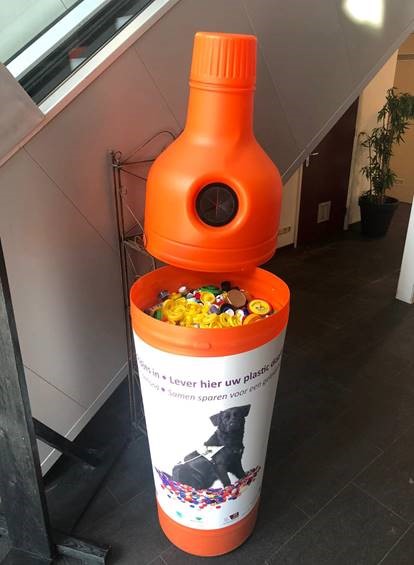 oranje plastic ton bij de OGtent (vorm van een fles) om plastic doppen in te leveren voor KNGF Geleidehonden