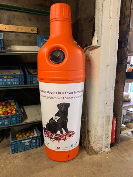 oranje plastic ton bij de Stokhorst (vorm van een fles) om plastic doppen in te leveren voor KNGF Geleidehonden